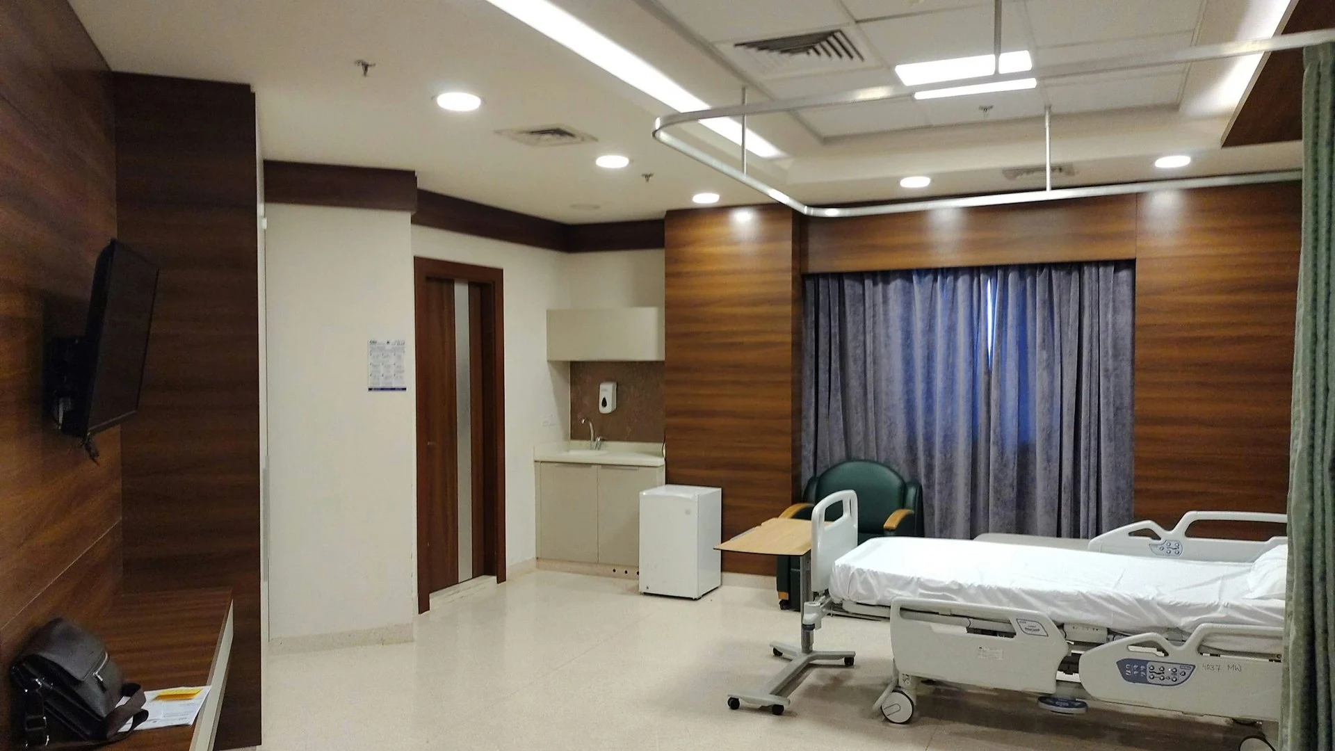 Kamar rawat inap rumah sakit dengan TV dinding dan tempat tidur pasien