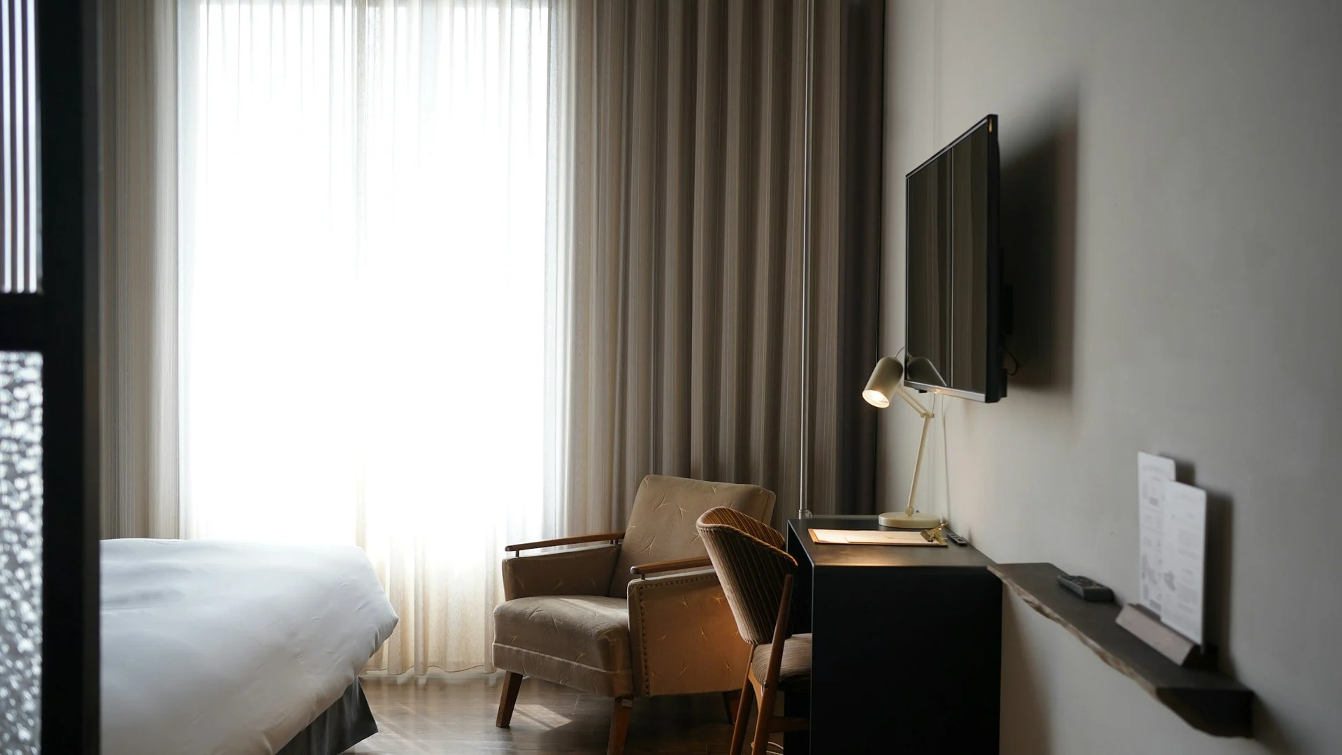 Kamar hotel butik dengan TV terpasang di dinding, kursi santai, dan meja kerja