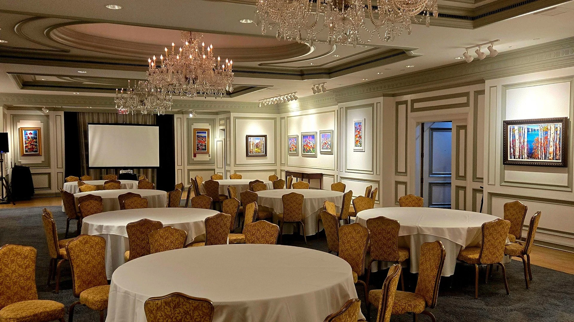 Ballroom hotel dengan meja bundar, lampu gantung, dan layar presentasi untuk acara MICE